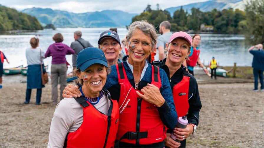 Four women in life-jackets at the waters edge smiling at the camera