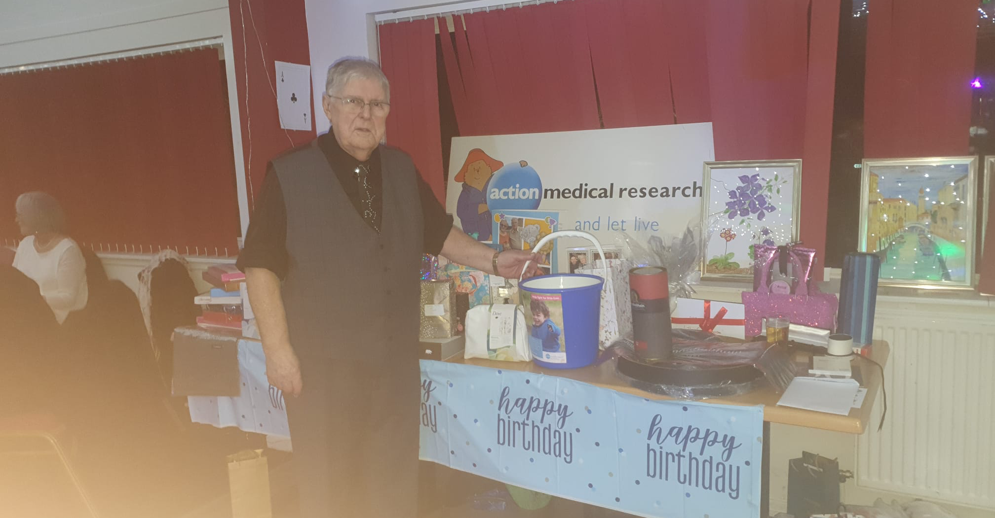 Hamish Wilson at his 90th birthday celebration, standing next to the Action donation bucket.
