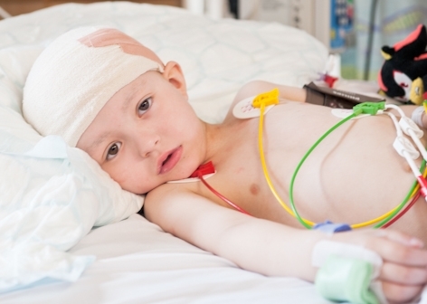 Joey in his hospital bed following surgery to remove his brain tumour. He has bandages wrapped around his head and several wires and pads on his chest