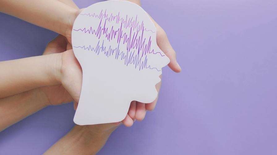 Hands holding encephalography (EEG) brain paper cutout as a visual representation of brain activity - EEG is used to detect and investigate epilepsy