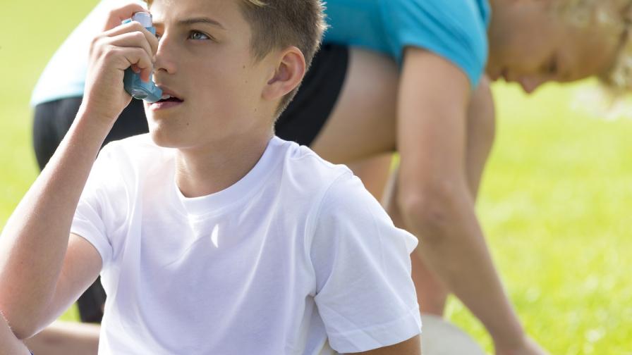 Teenage boy in sports clothes using a blue asthma inhaler.