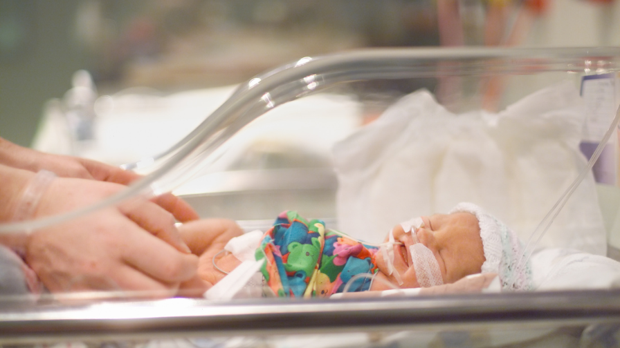 Baby lying on her back in a incubator whilst receiving breathing support