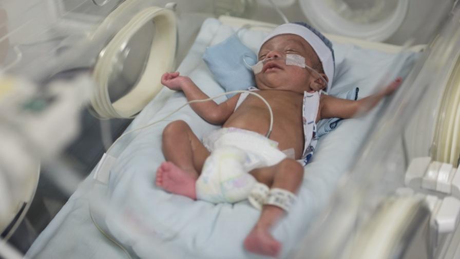 Premature baby boy laying in an incubator with a breathing tube.