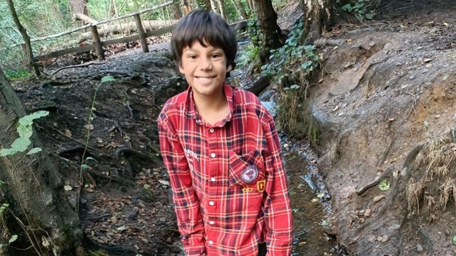 Robi, aged around 10, who has CDA-1 anaemia. He is standing in woodland, wearing a red-checked shirt.