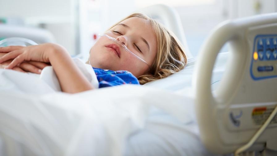 Sick child laying sleeping in a hospital bed, with a nasal tube to support breathing.