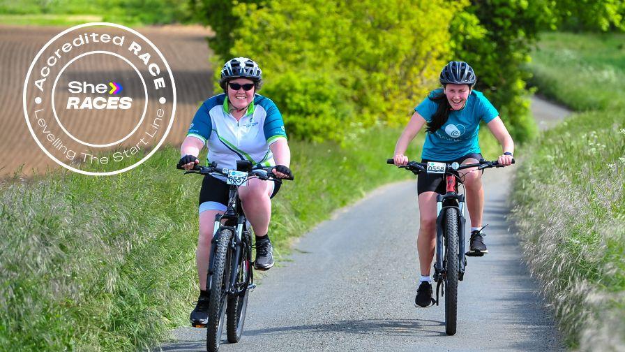 sheraces logo on an image of two women cycling