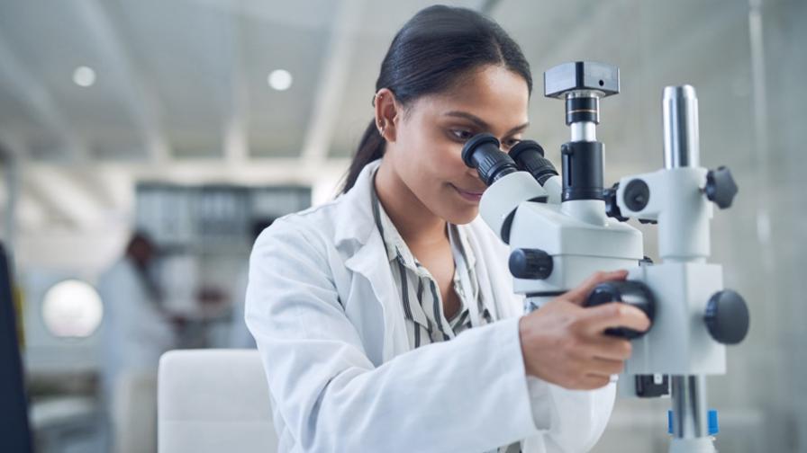 Female researcher in white lab coat looking into a microscope