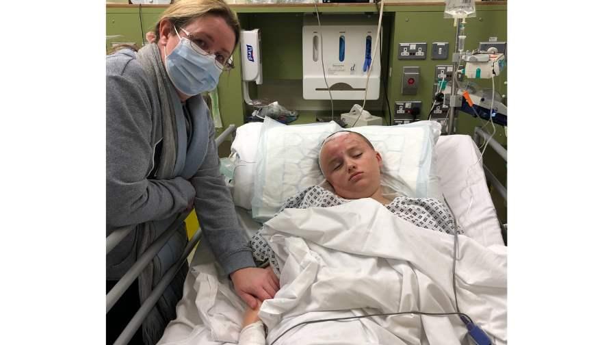 Image of Luke in hospital with his mum by his side wearing a facemask