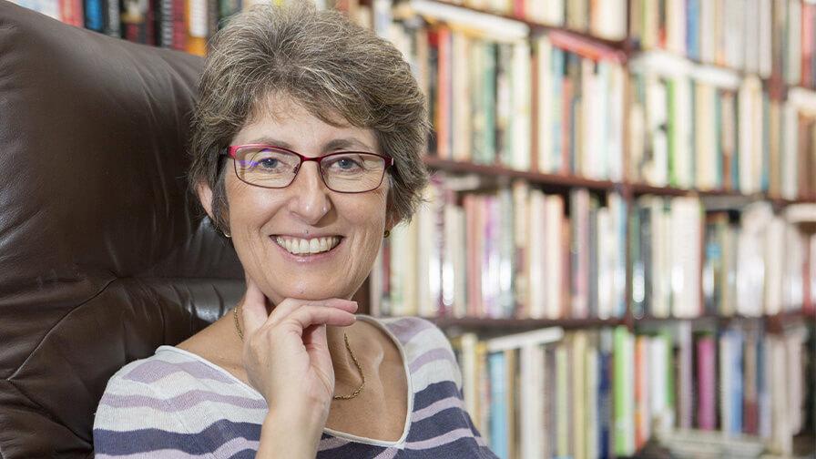 Karen Jankel smiling at the camera while sat in a high back chair with library shelves in the background