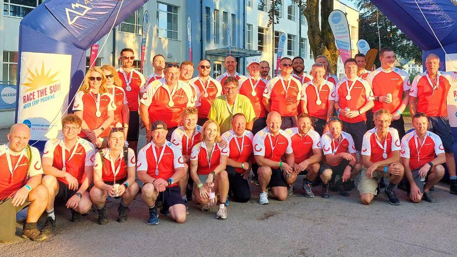 A large corporate team celebrating their completion of the Race the Sun challenge with medals and branded team kits