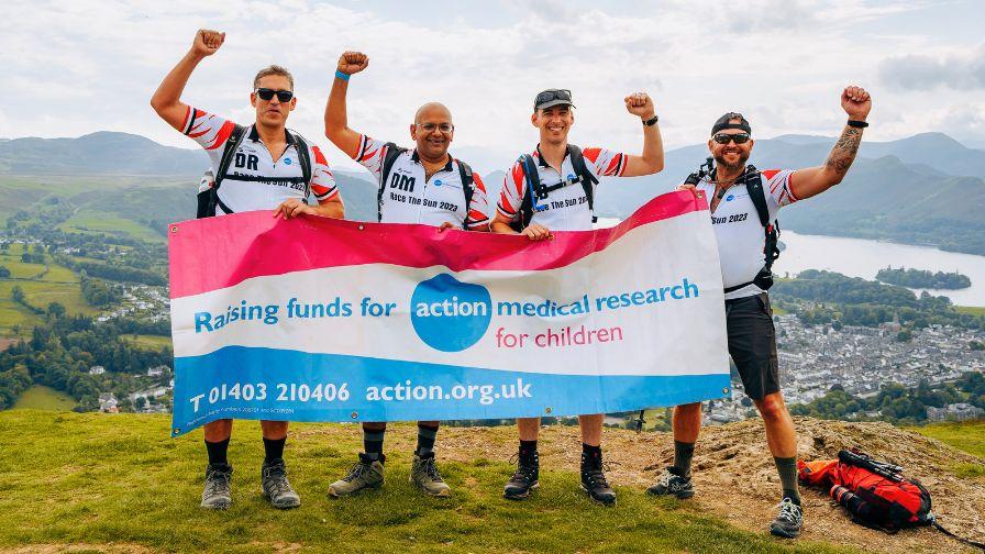 Teammates celebrate with a charity banner at a mountain summit during the Race the Sun challenge