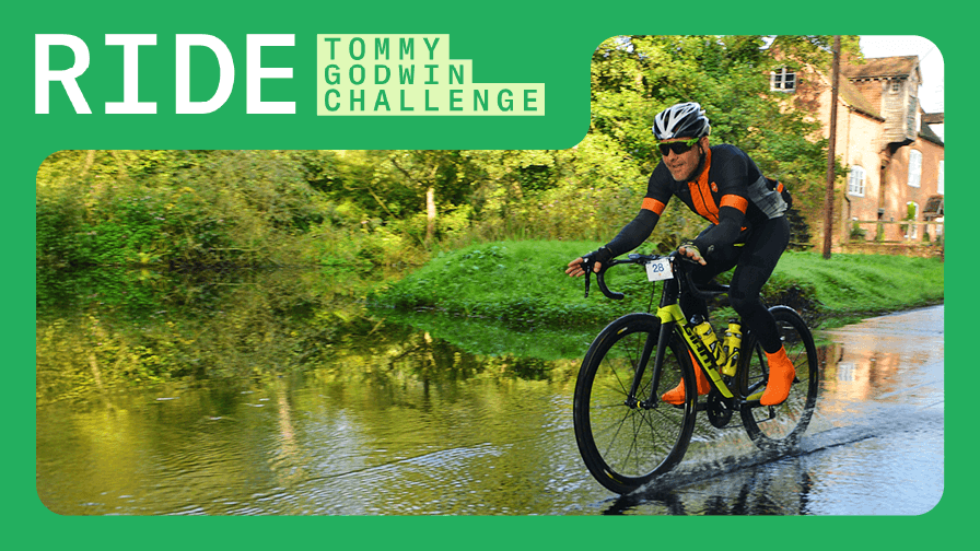 RIDE Tommy Godwin Challenge: A cyclist in orange and black gear rides through a flooded road next to a scenic canal.