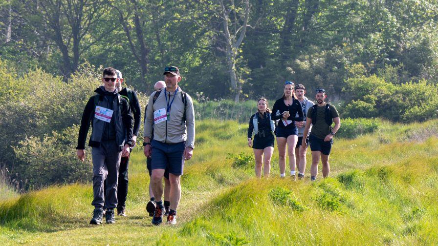 A group of people hiking together along a grassy trail through a scenic field.