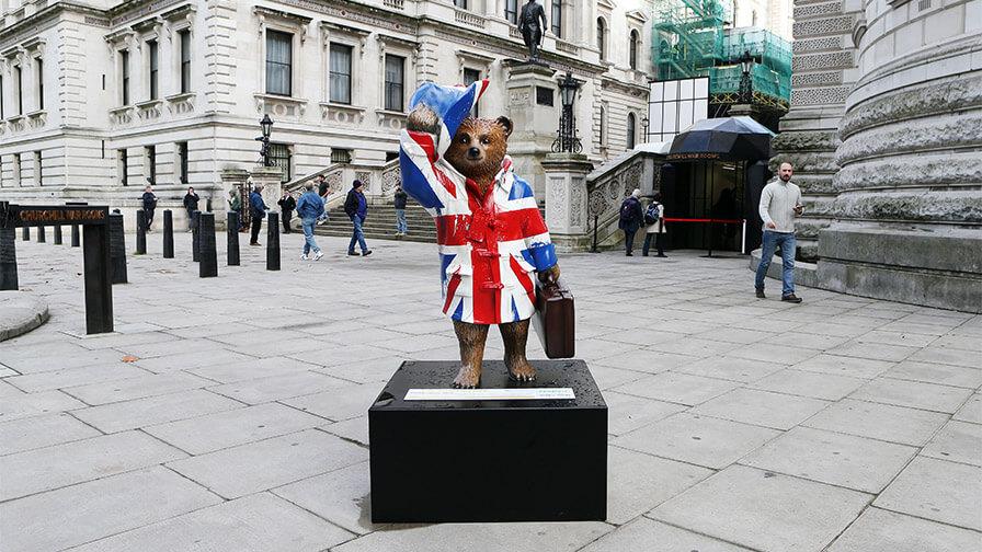 A statue of Paddington Bear painted with a Union Jack pattern stands on a black plinth in a London square.