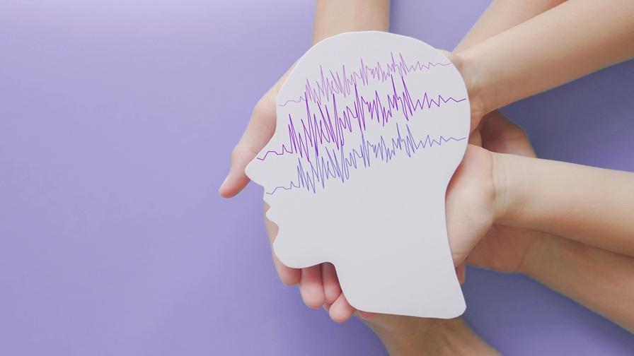 Adult and child hands against a light purple background, holding a cut-out illustration of the human brain with ECG lines on to show seizure activity.