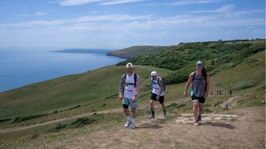 two male and one female participant walkin up hill with the dramatic jurassic coastline stretching out in the distance behind