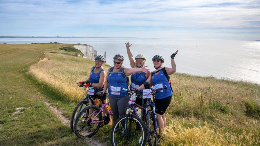 group of female cyclists posing with bikes on clifftop with arms in the air