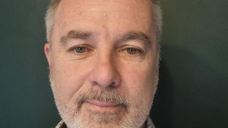 Headshot of a white man with light grey beard and short hair wearing a flowery shirt.