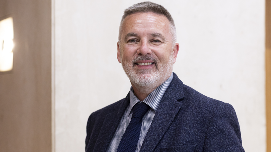 Headshot of a white man with light grey beard and short hair wearing a suit