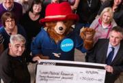 Person in Paddington Bear costume with an Action badge poses with a large check amoungst a crowd of office workers