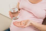 A pregnamr lady holding a tablet and glass of water