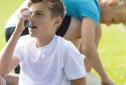 Teenage boy in sports clothes using a blue asthma inhale