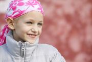 Young girl, who has lost her hair due to cancer treatment, wearing a pink head scarf.