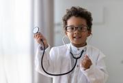 A smiling, young mixed race boy, aged about 5. He is wearing a glasses, a white doctor