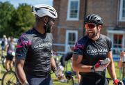 Two cyclists in Garmin cycling jerseys smiling and laughing while pushing their bikes after finishing ther ride