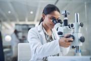 Female medical researcher, wearing a white lab coat and looking into a microscope.