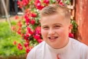 Digby standing in his garden in a white t-shirt, red rose bush in the background with a big smile on his face