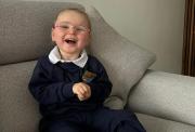 A young girl, aged about five, with Rett syndrome. She is propped up to sit on a sofa, wears glasses and is smiling.