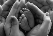 Black and white image of adult hands gently cradling a baby’s tiny feet, symbolizing love, care, and remembrance.