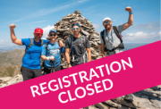 team of four stand on the summit of the old man of coniston with clear skies and views of the surrounding mountain range