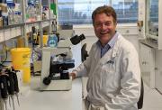 Dr Frederik van Delft sitting in a lab next to a microscope, with various medical equipment in the background. He is smiling and wearing a white lab coat.