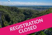 A scenic high-angle view of a lush, green gorge and a distant town, with a bright pink diagonal banner across the foreground that reads "REGISTRATION CLOSED" in bold white text