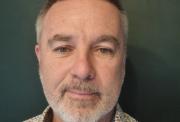 Headshot of a white man with light grey beard and short hair wearing a flowery shirt.