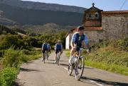 Riders on a quiet Spanish road with a church and mountains behind them; no cars