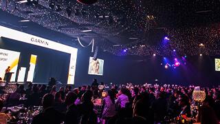 Panaramic photo of the gala dinner showing a person on stage speak to a large room of people sat at dinner tables