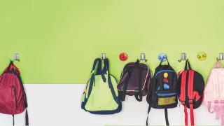 A row of childrens rucksacks hanging on hooks in a school hallway