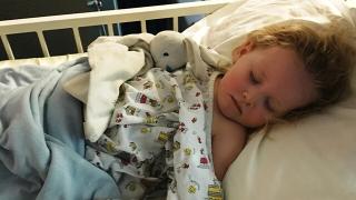 Georgia laying asleep in a hospital bed with rabit teddy
