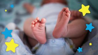 Close-up of a baby lying down with tiny feet in focus, surrounded by colorful blue and yellow star graphics on a soft blanket.