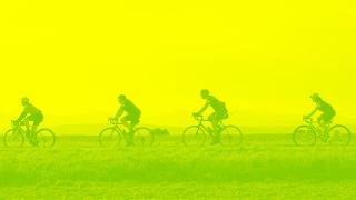 Four cyclists ride in a line through a scenic mountain landscape, tinted with a yellow-green gradient to suggest motion and energy.