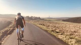cyclist riding into a golden sunset along a stretch of rural road
