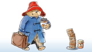 An illustration of Paddington Bear carrying a suitcase and a jar of marmalade next to a stack of sandwiches.