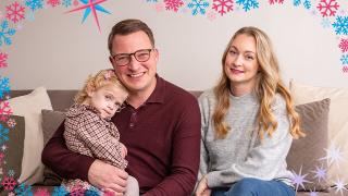 A smiling family with a young daughter sitting together on a couch, framed by a festive snowflake border.