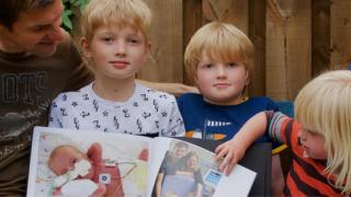 Elijah's Mum, Dad and siblings on a garden bench diaplaying a photo album of Elijah