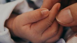 A newborn babys hand holding onto a grown-up finger