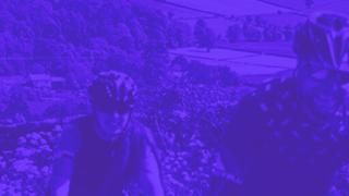 A close-up shot of five cyclists riding up a steep hill in the countryside with a deep purple filter.