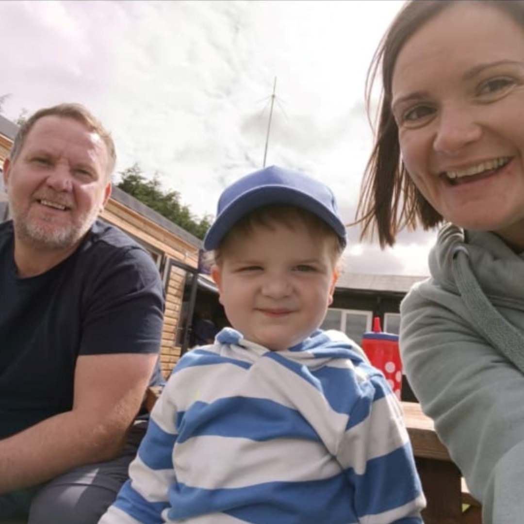 Image of Evan smiling with his mum and dad